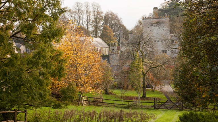 View of the abbey and barn in autumn from the woods beyond garden house at Buckland Abbey, Devon